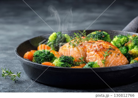 Steamed fish with with broccoli, carrot hot black pan. Baked salmon gray background. Paleo, keto, lshf, or dash diet. Fish and vegetables. Oven dish, gluten free, clean eating, balanced healthy food. 130812766