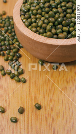 Close-up of green mung beans in a wooden bowl with scattered beans on wooden background, representing plant protein, healthy eating, and Asian cuisine ingredient. Close-up of green mung beans in a wooden bowl with scattered beans on wooden background, representing plant protein, healthy eating, and Asian cuisine ingredient. 130812978