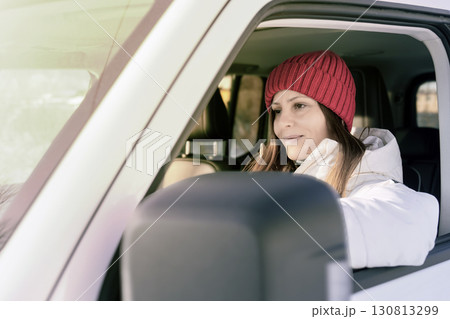 Woman wearing a red beanie sitting in a vehicle enjoying a winter drive in a scenic area during the afternoon 130813299