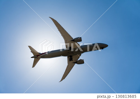 まぶしい太陽と青空の下を通過していく旅客機　ロンドン郊外のヒースロー空港近くにて 130813685