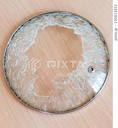 damaged glass lid with metal rim, shattered with pieces missing, is sitting on light colored wooden surface 130813852