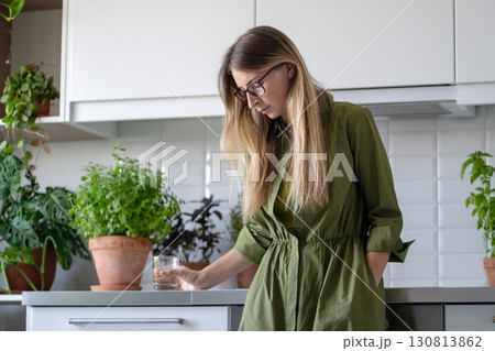 Thoughtful weak woman drink water with medication in kitchen early morning, fatigue and low energy Thoughtful weak woman drink water with medication in kitchen early morning, fatigue and low energy 130813862