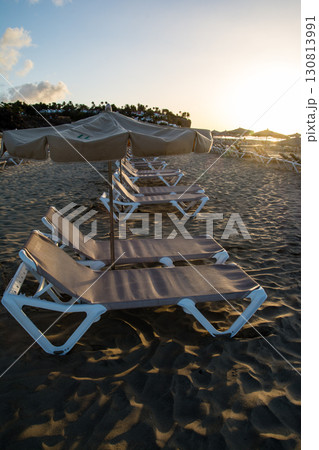 朝日を浴びる海岸線の砂浜に並べられたビーチベッドとパラソル　カナリア諸島のフエルテベンテュラ島にて 130813991