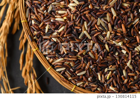 Top view of organic mixed rice grains in a bamboo basket with golden rice ears  on black stone 130814115