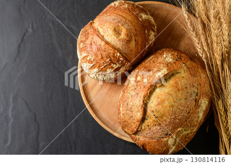 Top view of a freshly baked, crusty artisanal sourdough loaf, presented on a rustic wooden plate. Top view of a freshly baked, crusty artisanal sourdough loaf, presented on a rustic wooden plate. 130814116