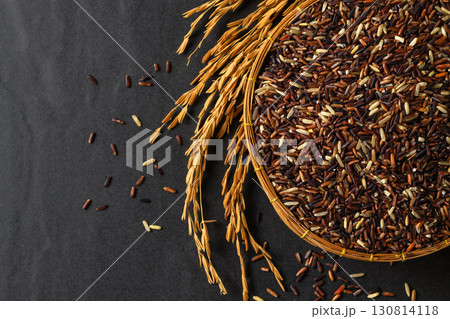 Top view of organic mixed rice grains in a bamboo basket with golden rice ears  on black stone Background. 130814118
