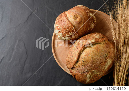 Top view of a freshly baked, crusty artisanal sourdough loaf, presented on a rustic wooden plate. 130814120