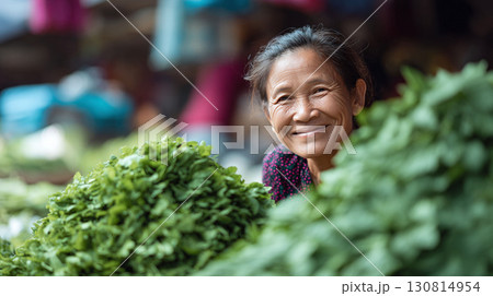 Warm portrait of a smiling vendor at a local market, surrounded by fresh green produce. Authentic culture, healthy lifestyle, and community concepts. 130814954