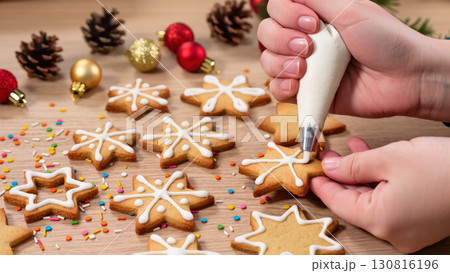 Christmas cookies being decorated with white icing by hand on wooden table with festive ornaments and sprinkles 130816196
