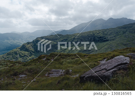 Majestic mountains rise above a foreground of vibrant green grass and a large, weathered rock. A tranquil scene of untouched natural beauty. 130816565
