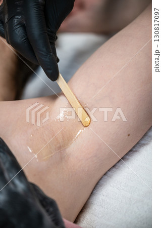 Beautician applying wax with wooden spatula on female armpit during professional hair removal procedure 130817097