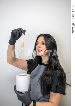 Beautician woman in black gloves holding jar of sugaring paste for hair removal procedure 130817103