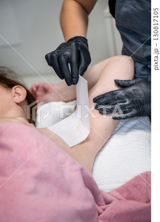 Beautician applying wax strip on female armpit during professional hair removal procedure Beautician applying wax strip on female armpit during professional hair removal procedure 130817105