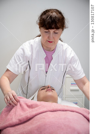 Beautician preparing female client for cosmetic facial treatment in professional beauty salon 130817107