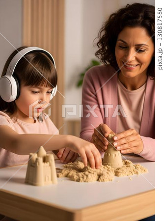 Neurodivergent kid girl in sensory therapy with white headphones playing with kinetic sand guided by therapist for tactile skills autism awareness and inclusion 130817580