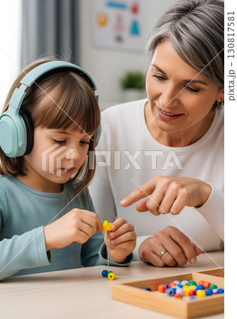 Autistic child girl in occupational therapy with turquoise headphones threading colorful beads for fine motor skills autism spectrum learning and inclusion awareness 130817581