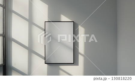 Black frame with a blank white canvas on a white wall in bright natural light and window shadow play 130818220