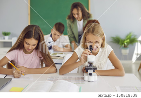 School girl working in class with microscope while her classmate making notes during a lesson School girl working in class with microscope while her classmate making notes during a lesson 130818539