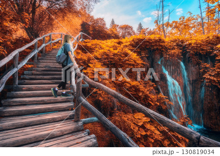 Woman with backpack walking on wooden path. Waterfalls in autumn 130819034
