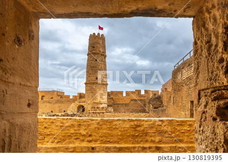 View through arch to the watch tower with tunisian flag on the top of Ribat of Monastir under cloudy skies, Monastir, Monastir Governorate, Tunisia 130819395