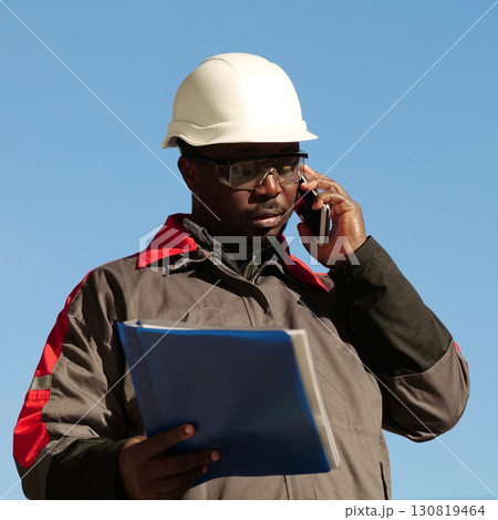 African american builder with work papers talks on smartphone African american builder with work papers talks on smartphone 130819464