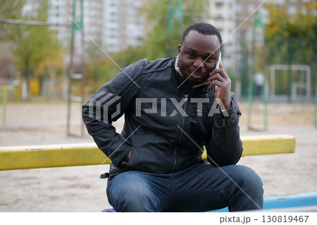 African american man sits at sport ground and speaks on smartphone African american man sits at sport ground and speaks on smartphone 130819467