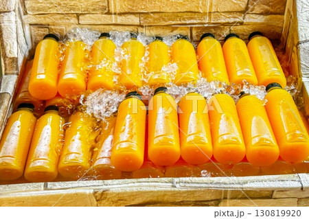 Rows of fresh orange juice in transparent bottles are chilled in water-filled, makeshift street cooler, showcasing a refreshing, healthy, summer beverage in vibrant street market setting Rows of fresh orange juice in transparent bottles are chilled in water-filled, makeshift street cooler, showcasing a refreshing, healthy, summer beverage in vibrant street market setting 130819920