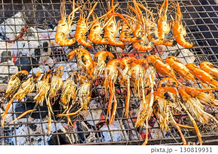 Tasty grilled prawns on wire rack sizzle, exuding smoky allure at a street food stall, promising a tasty, healthful seaside snack to passersby and seafood enthusiasts. Seafood. Wild feasting concept 130819931