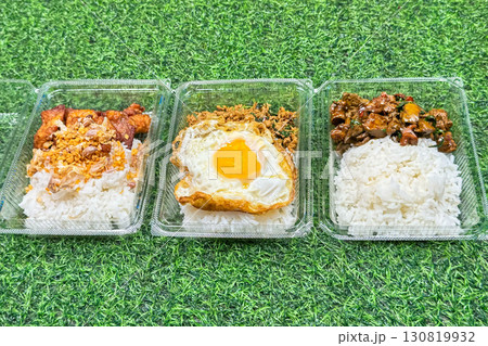Takeaway containers showcase popular street food meals with rice, each topped with different options, crispy pork, egg, and savory beef, highlighting convenience and variety in urban eating 130819932