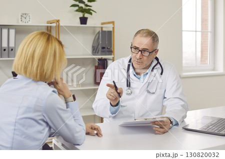 Middle aged doctor therapist consulting patient in medical office Middle aged doctor therapist consulting patient in medical office 130820032