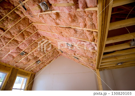 Insulation is being installed in roof of residential building with visible wooden beams recessed lights. 130820103