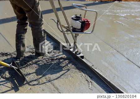 Construction worker uses power trowel to create smooth concrete surface on works day. 130820104