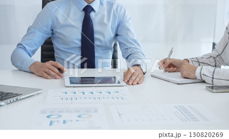 Business professionals analyzing financial charts, graphs on tablet and laptop, collaborating closely during strategic planning session in contemporary workspace Business professionals analyzing financial charts, graphs on tablet and laptop, collaborating closely during strategic planning session in contemporary workspace 130820269