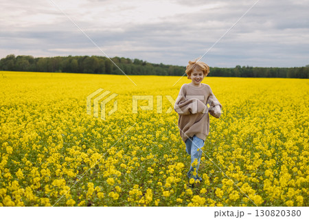 Smiling 9 year old girl in oversize sweater running in yellow rapeseed field Smiling 9 year old girl in oversize sweater running in yellow rapeseed field 130820380