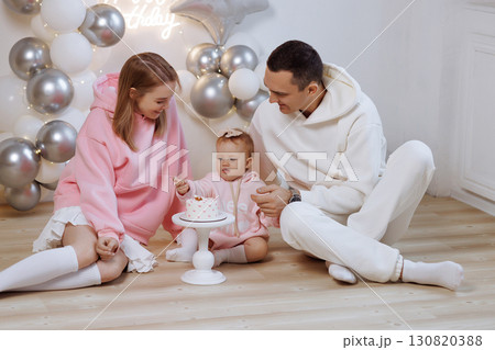 Happy family with baby celebrating birthday at home with balloons, cake and wooden floor Happy family with baby celebrating birthday at home with balloons, cake and wooden floor 130820388