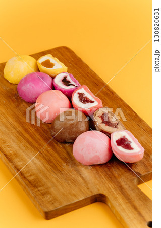 Assorted mochi ice cream on wooden board over vibrant yellow background, flat lay 130820631
