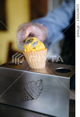 Hand scooping mango ice cream into waffle cone at artisan gelato shop, close up view 130820655