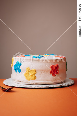 Handmade celebration cake with colorful floral buttercream decorations on orange background 130820659