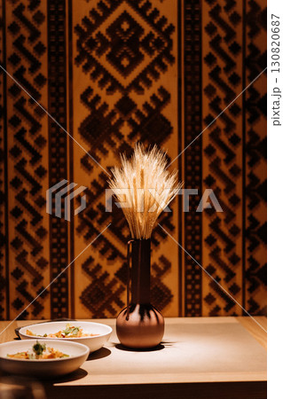 Traditional wheat bouquet in a clay vase with ethnic background and warm cozy lighting Traditional wheat bouquet in a clay vase with ethnic background and warm cozy lighting 130820687