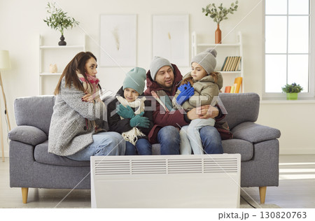 Unhappy parents, small children freezing at home wearing winter warm clothes near radiator Unhappy parents, small children freezing at home wearing winter warm clothes near radiator 130820763