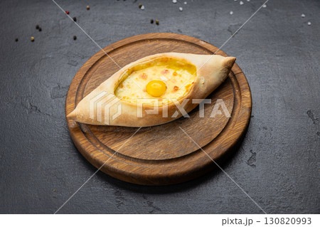 Traditional Georgian Adjarian khachapuri with eggs and cheese on a wooden board Traditional Georgian Adjarian khachapuri with eggs and cheese on a wooden board 130820993