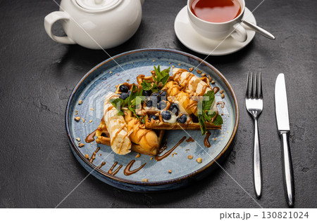 Belgian waffles with caramel, banana, berries and tea on a black stone background 130821024