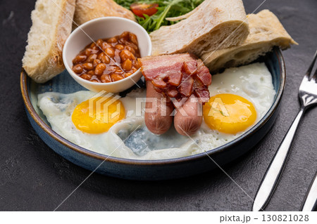 Traditional English breakfast with eggs, bacon, beans, toast, and tea on a dark background 130821028