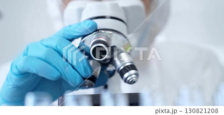 Professional scientist in protective gear is using microscope in a laboratory setting, close-up. Science and medicine concepts Professional scientist in protective gear is using microscope in a laboratory setting, close-up. Science and medicine concepts 130821208