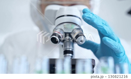 Professional scientist in protective gear is using microscope in a laboratory setting, close-up. Science and medicine concepts 130821216