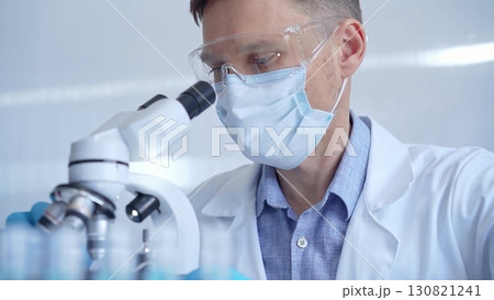 Man scientist with protective glasses, mask and gloves is using microscope in laboratory, portrait of researcher. Microbiology science concept 130821241