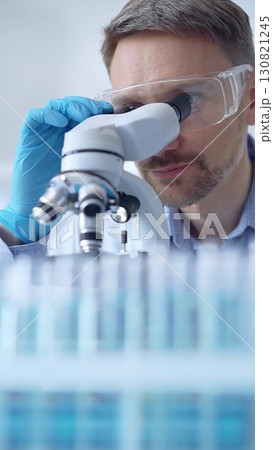Man scientist with protective glasses and gloves is using microscope in laboratory, vertical portrait of researcher. Microbiology science concept 130821245