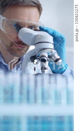 Man scientist with protective glasses and gloves is using microscope in laboratory, vertical portrait of researcher. Microbiology science concept 130821273
