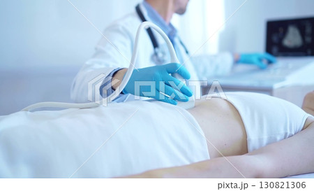 Doctor man wearing a blue medical gloves using an ultrasound equipment on a female patient lying down in clinic cabinet. Medicine concept 130821306