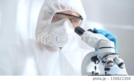 Scientist is analyzing samples using a microscope in a laboratory setting. Close-up of a focused researcher in a protective gear. Science concept 130821308